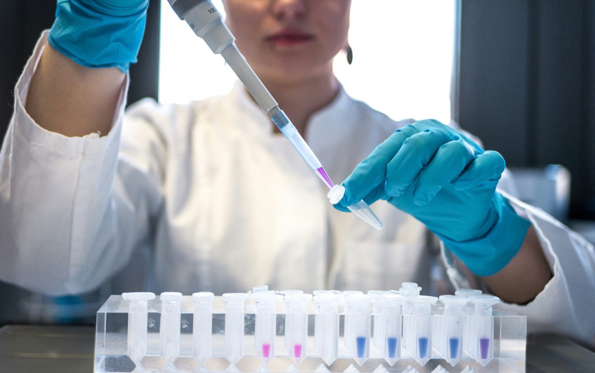 Analista de laboratorio con pipeta multicanal sobre una fila de viales, en pleno análisis de identidad y pureza