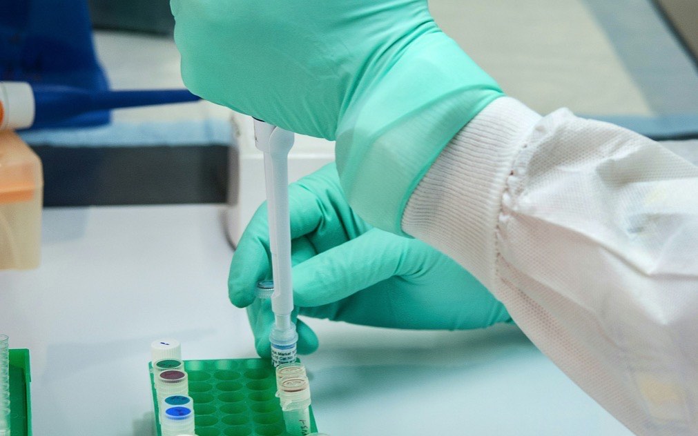 Investigador dosificando líquido con una pipeta sobre viales de laboratorio